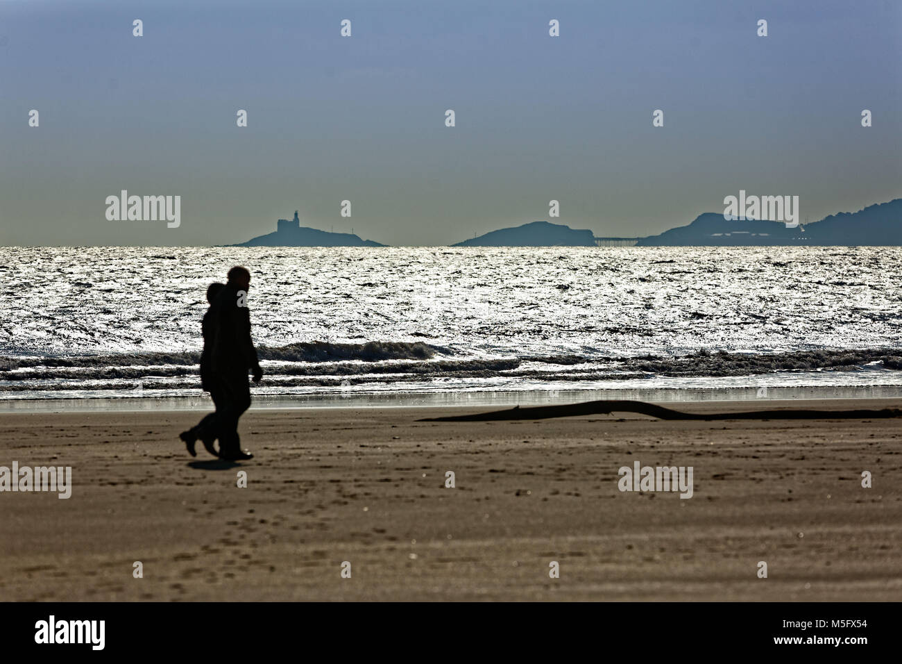 Nella foto: un paio di camminare sulla spiaggia e si affaccia Mumbles a Swansea lungomare in Galles, NEL REGNO UNITO. Venerdì 23 Febbraio 2018 Re: parti del Regno Unito sono state godere Foto Stock