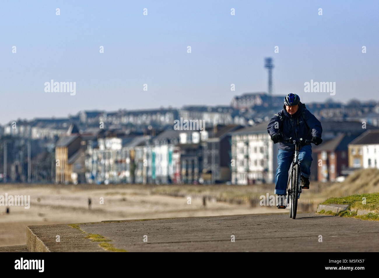 Nella foto: un uomo cicli a Swansea lungomare in Galles, NEL REGNO UNITO. Venerdì 23 Febbraio 2018 Re: parti del Regno Unito sono state godendo il sole con un freddo cane te Foto Stock