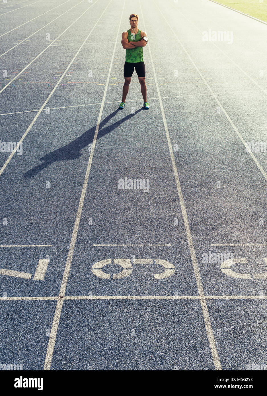 Runner permanente sulla via di corsa con le mani piegate. Atleta che indossa auricolari con telefono mobile fissato nella fascia braccio. Foto Stock