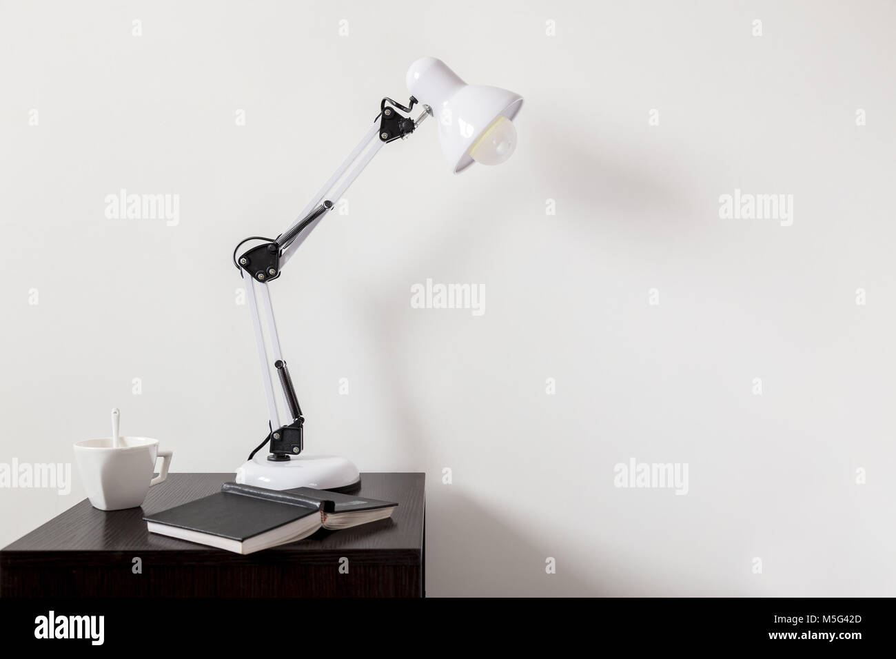La lampada bianca sul monitor al posto letto accanto a un libro e una tazza di tè Foto Stock