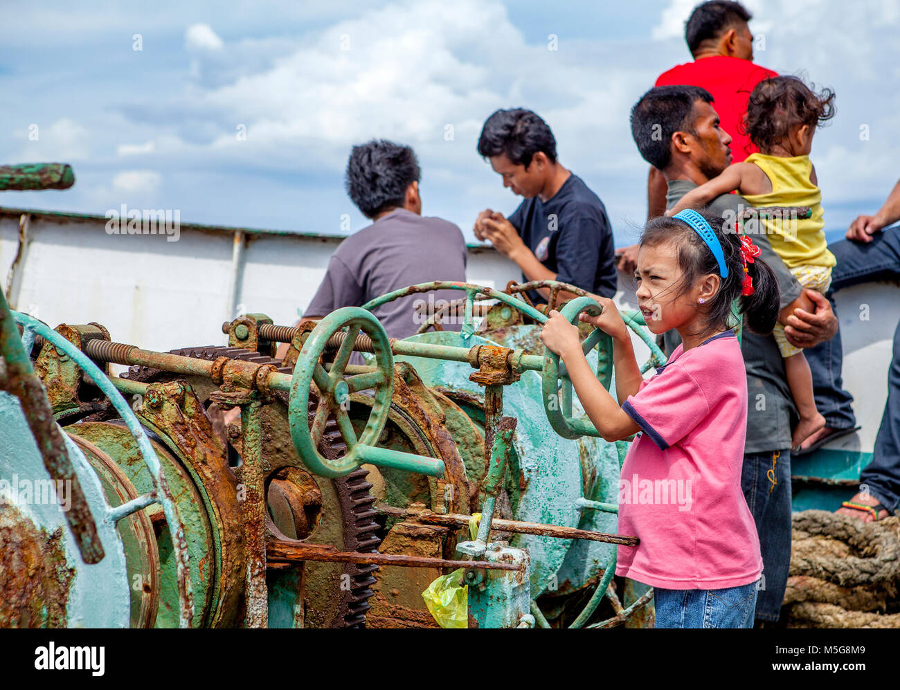 Una giovane ragazza filippina a bordo di un traghetto per le isole finge di guidare la barca da giocare con vecchi machienery sul ponte mentre si è in viaggio da Cebu a Bohol, Ph Foto Stock