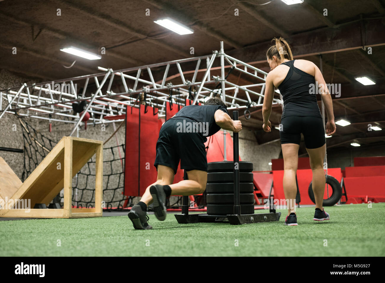 Trainer femminile aiutando l uomo con slitta spingendo Foto Stock