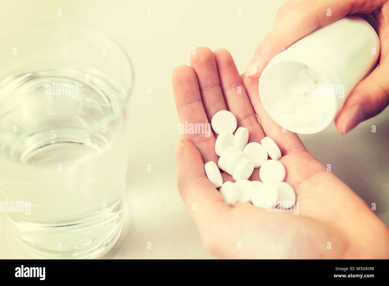 Concetto di immagine di farmaci dipendenze - mano della giovane donna con molte pillole e acqua in close-up (effetto vintage). Foto Stock