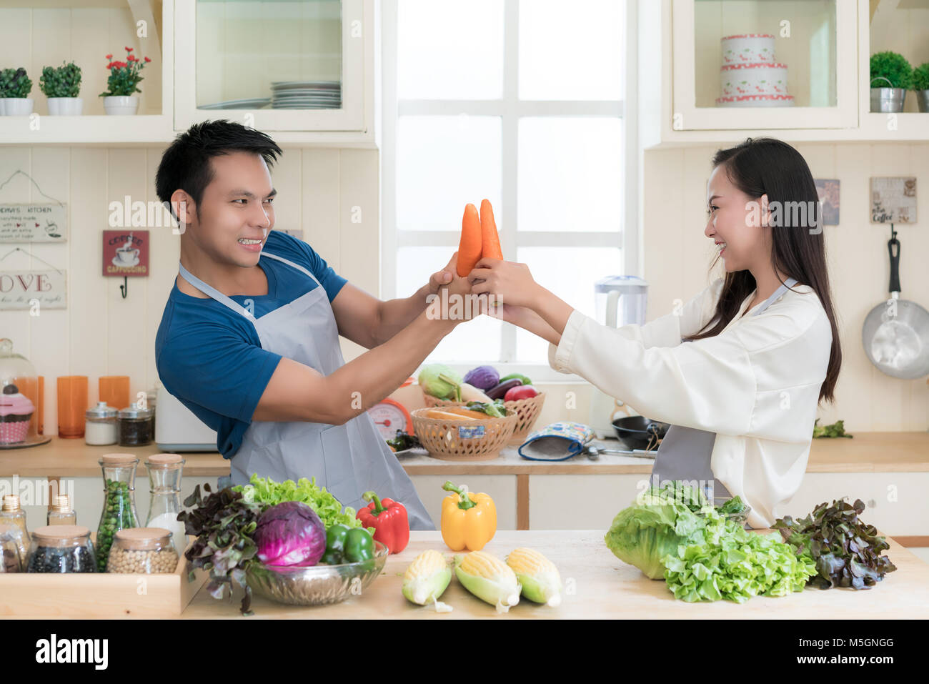 Divertimento Asian giovane lotta simulata con le carote come Asian giovane cuoco pasto sano insieme usando verdure fresche ed erbe aromatiche. Foto Stock