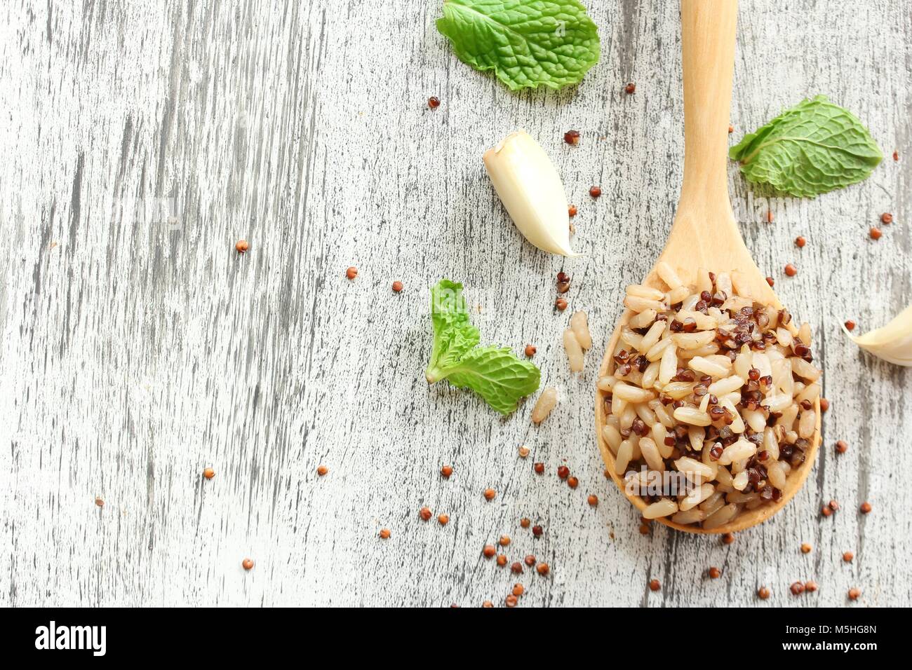 Cuocere la quinoa riso marrone in un cucchiaio di legno rustico sfondo bianco, il fuoco selettivo Foto Stock