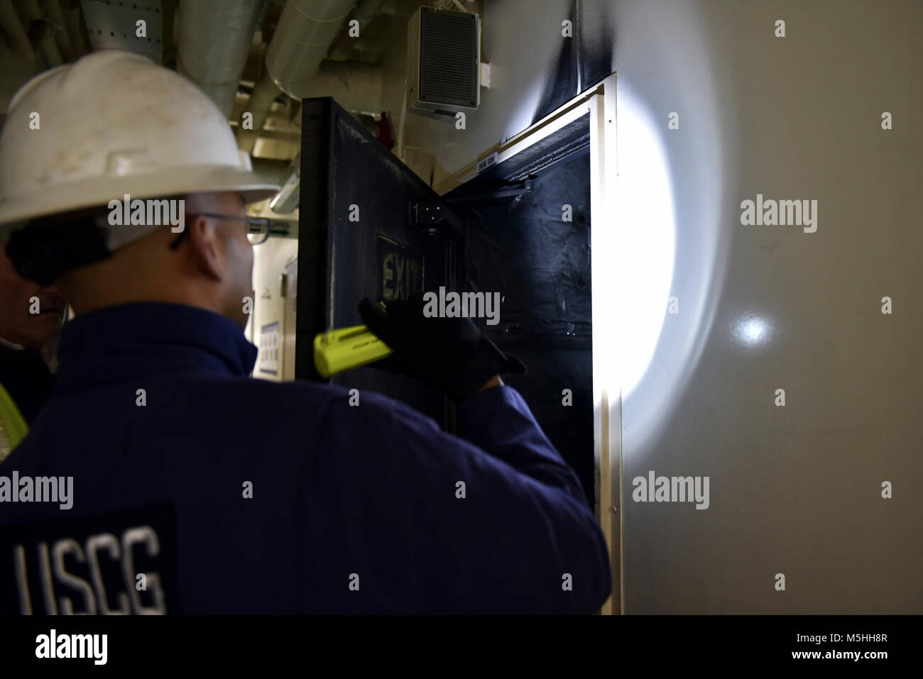 Una guardia costiera settore Puget Sound investigatore marino esamina una porta antincendio a bordo della 876 piedi di portacontainer MOL PRESTIGE il 12 febbraio 2018, presso il Molo 18 nel porto di Seattle mentre lavora su indagini preliminari sulle cause della sala motori Fire come ha iniziato il suo viaggio a Tokyo in Giappone, il 1 febbraio. La guardia costiera conduce una media di più di 70.000 recipiente interno ispezioni e 10.000 del controllo dello Stato di approdo esami di navi straniere conformemente alle normative federali. Stati Uniti Coast Guard Foto Stock