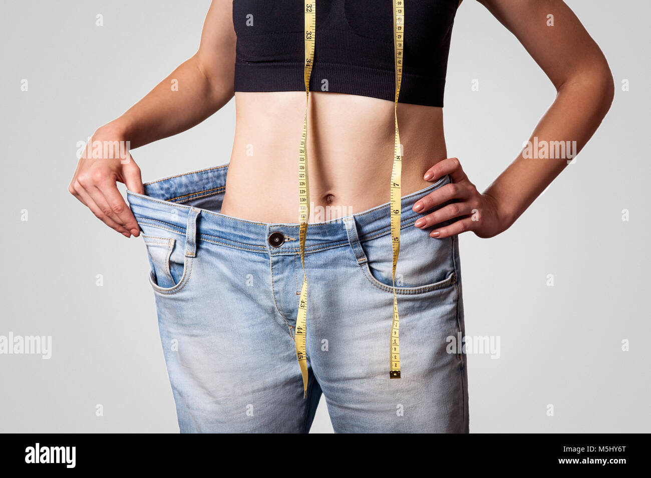 Close-up di slim in vita della giovane donna in jeans grandi mostra di successo di perdita di peso, isolato su sfondo grigio chiaro, dieta concetto. Foto Stock