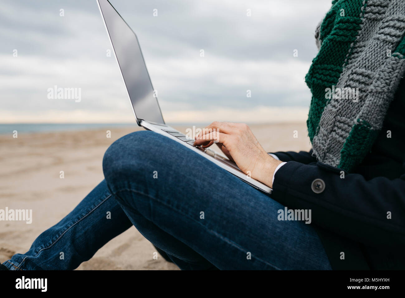 Imprenditore seduto sulla spiaggia in inverno utilizzando laptop, vista parziale Foto Stock