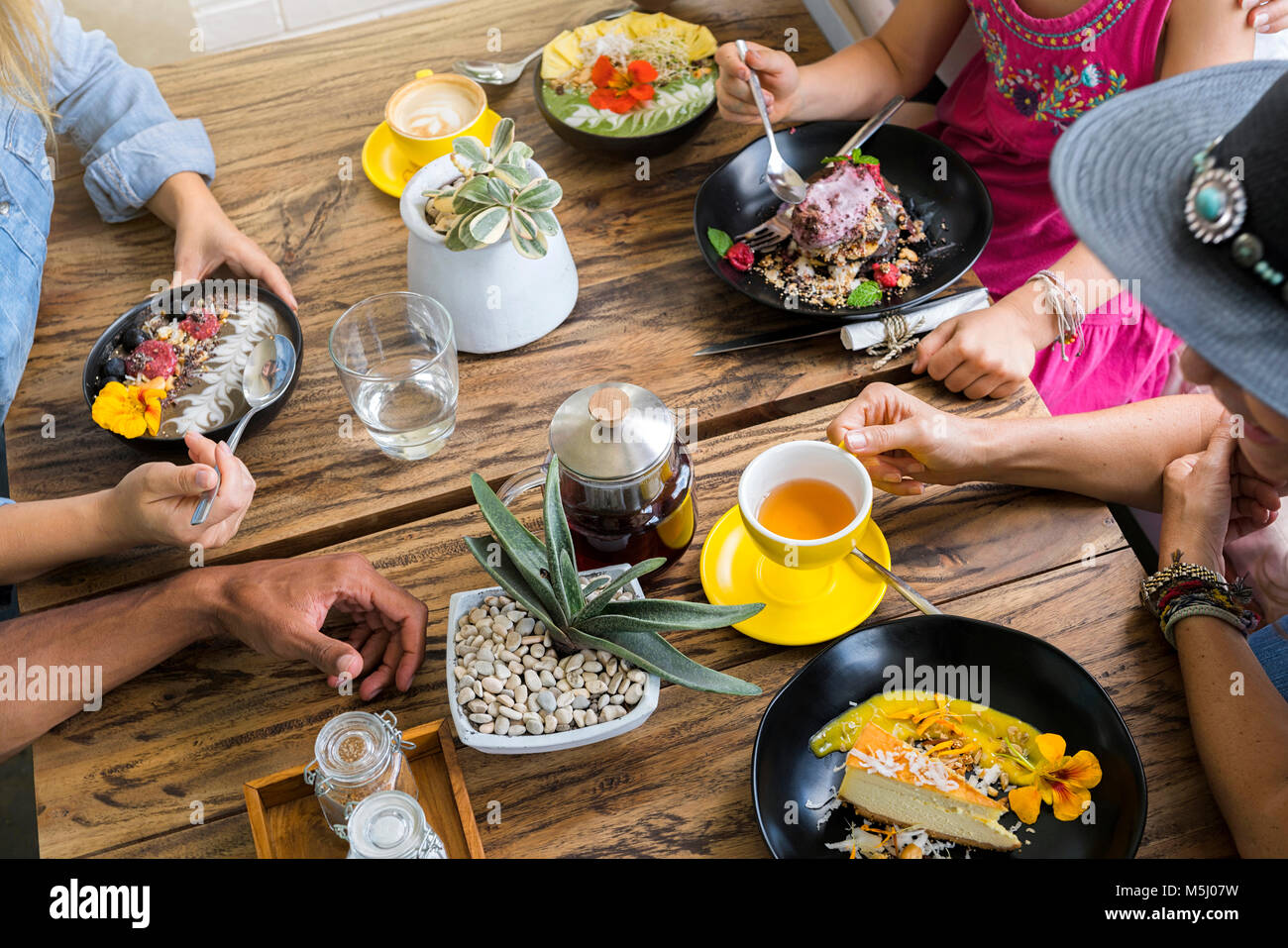 Persone raccogliendo attorno a un tavolo di legno bere e mangiare cibo vari Foto Stock