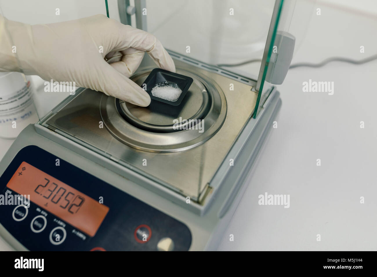 Mano con guanto protettivo utilizzando scale in laboratorio di una farmacia Foto Stock