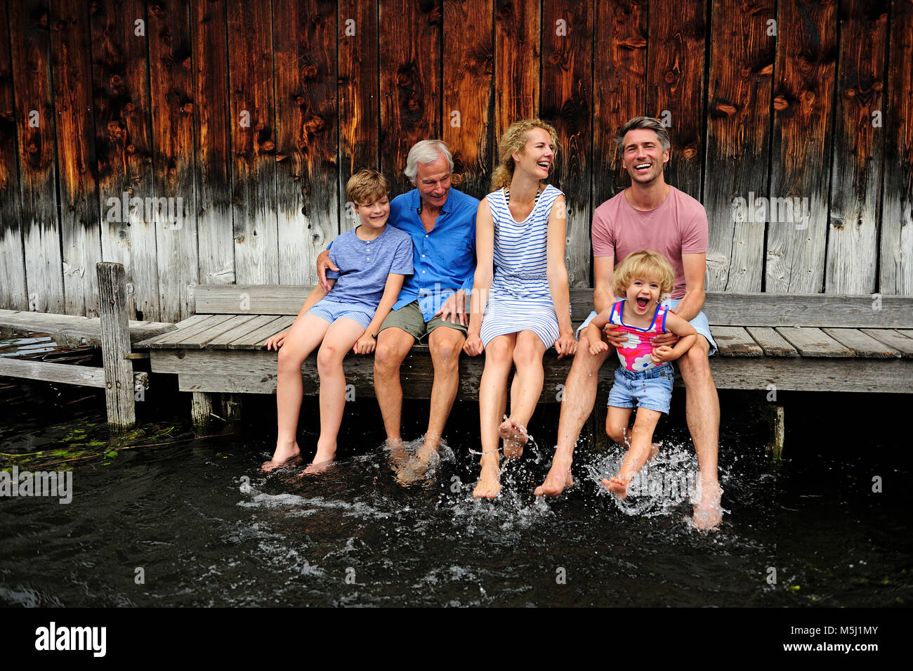 Famiglia seduti insieme su jetty schizzi con acqua Foto Stock