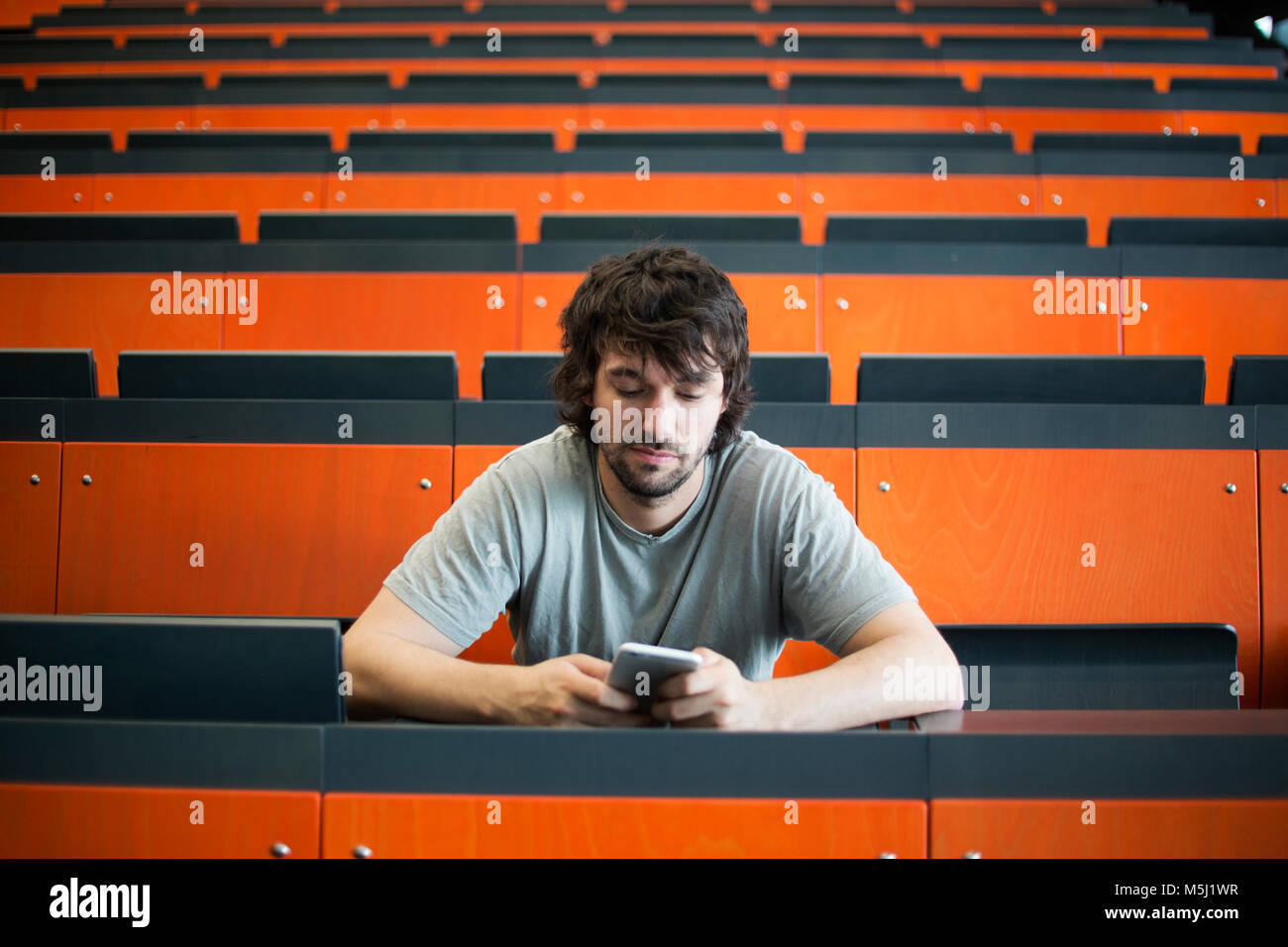 Ritratto di studente in auditorium presso università guardando al telefono cellulare Foto Stock