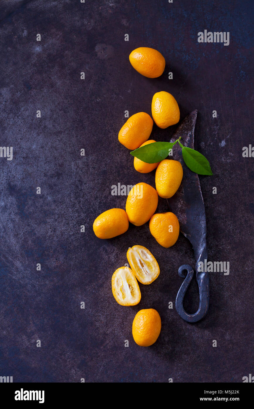 Affettato e tutto il kumquat, foglie e vecchio coltello sulla terra arrugginito Foto Stock
