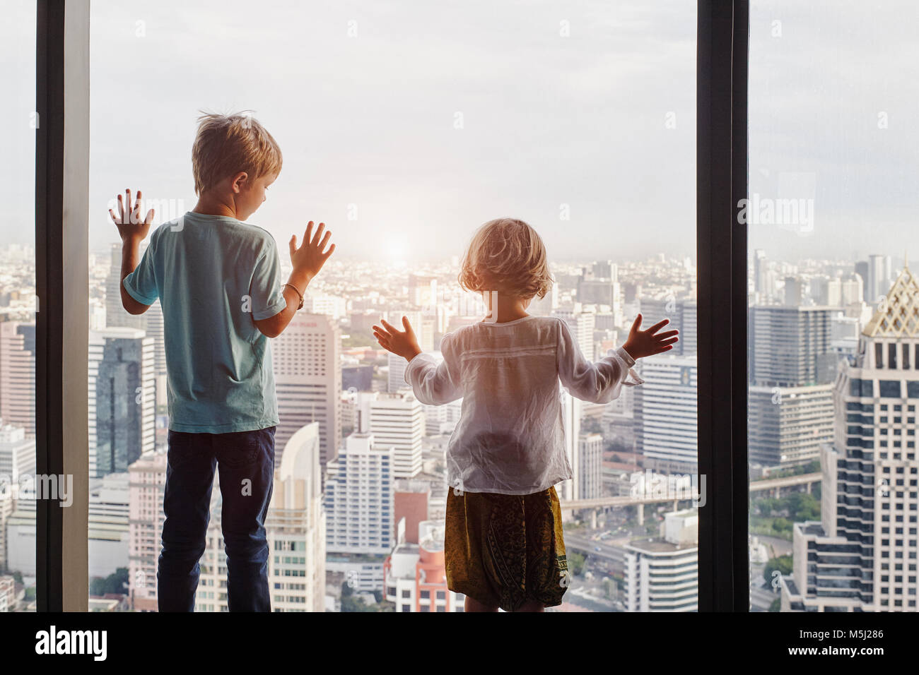 Thailandia, Bangkok, bambino e bambina guardando attraverso la finestrella a cityscape Foto Stock