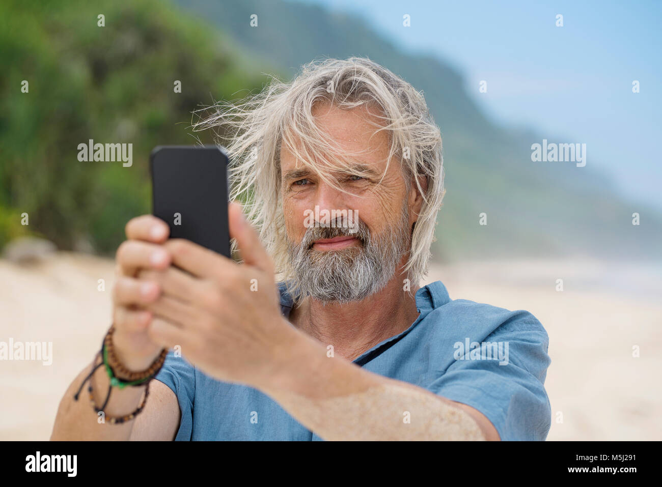 Bel uomo senior di scattare una foto con lo smartphone sulla spiaggia Foto Stock