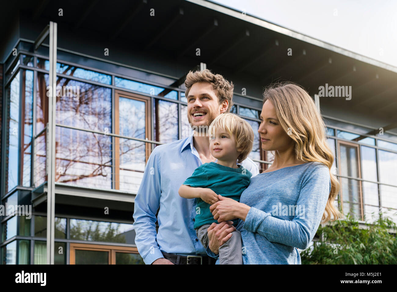 Sorridente genitori con figlio davanti alla loro casa Foto Stock