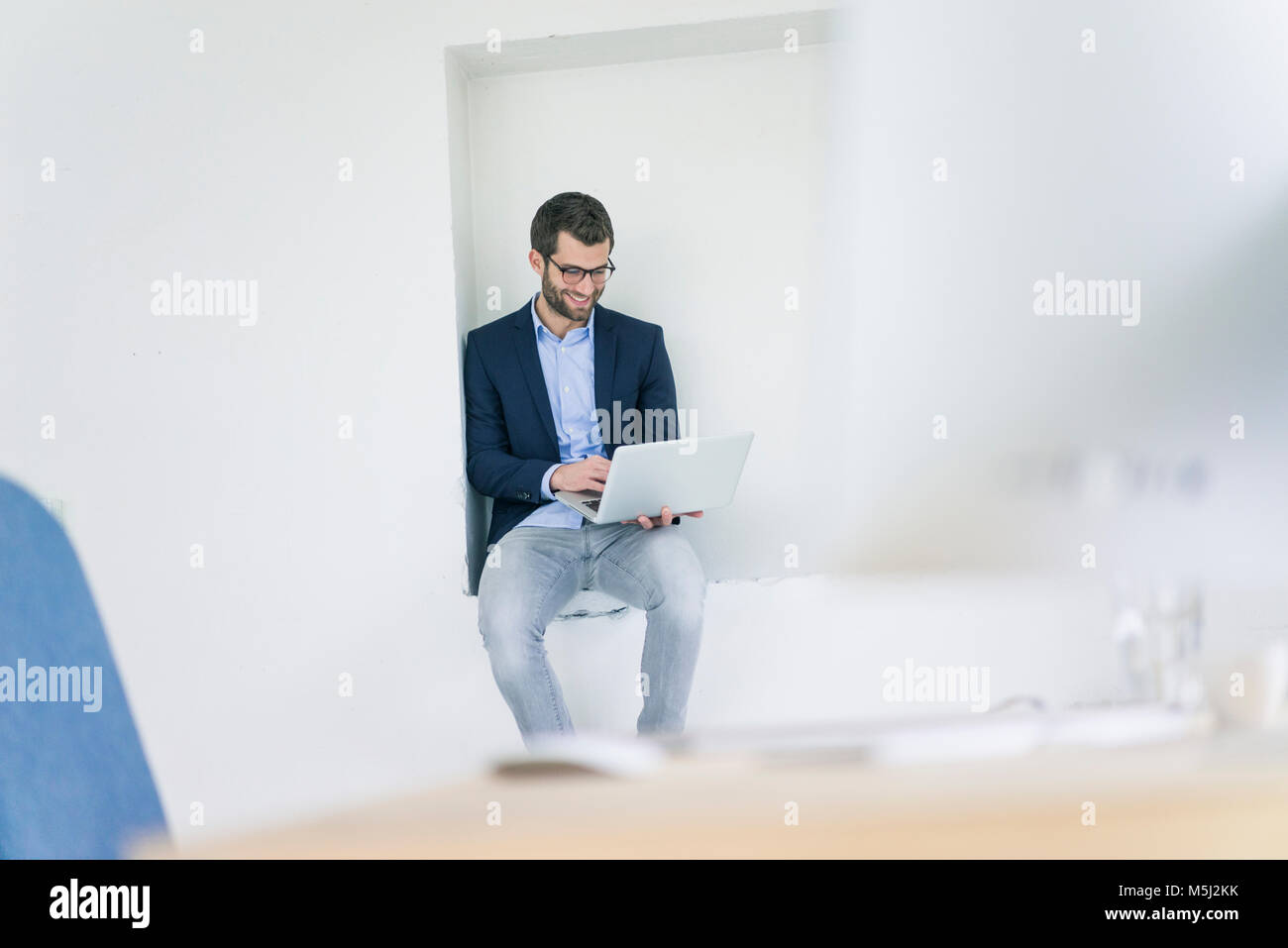 Imprenditore sorridente seduto in una nicchia con laptop Foto Stock