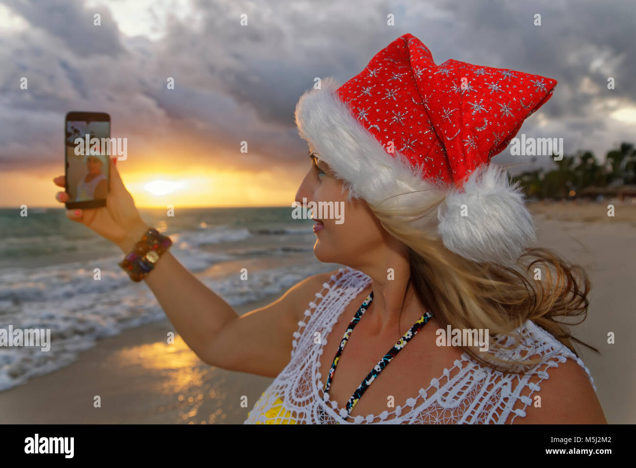 Caraibi, Repubblica Dominicana, Punta Cana, donna con cappello di Natale tenendo selfie sulla spiaggia Foto Stock