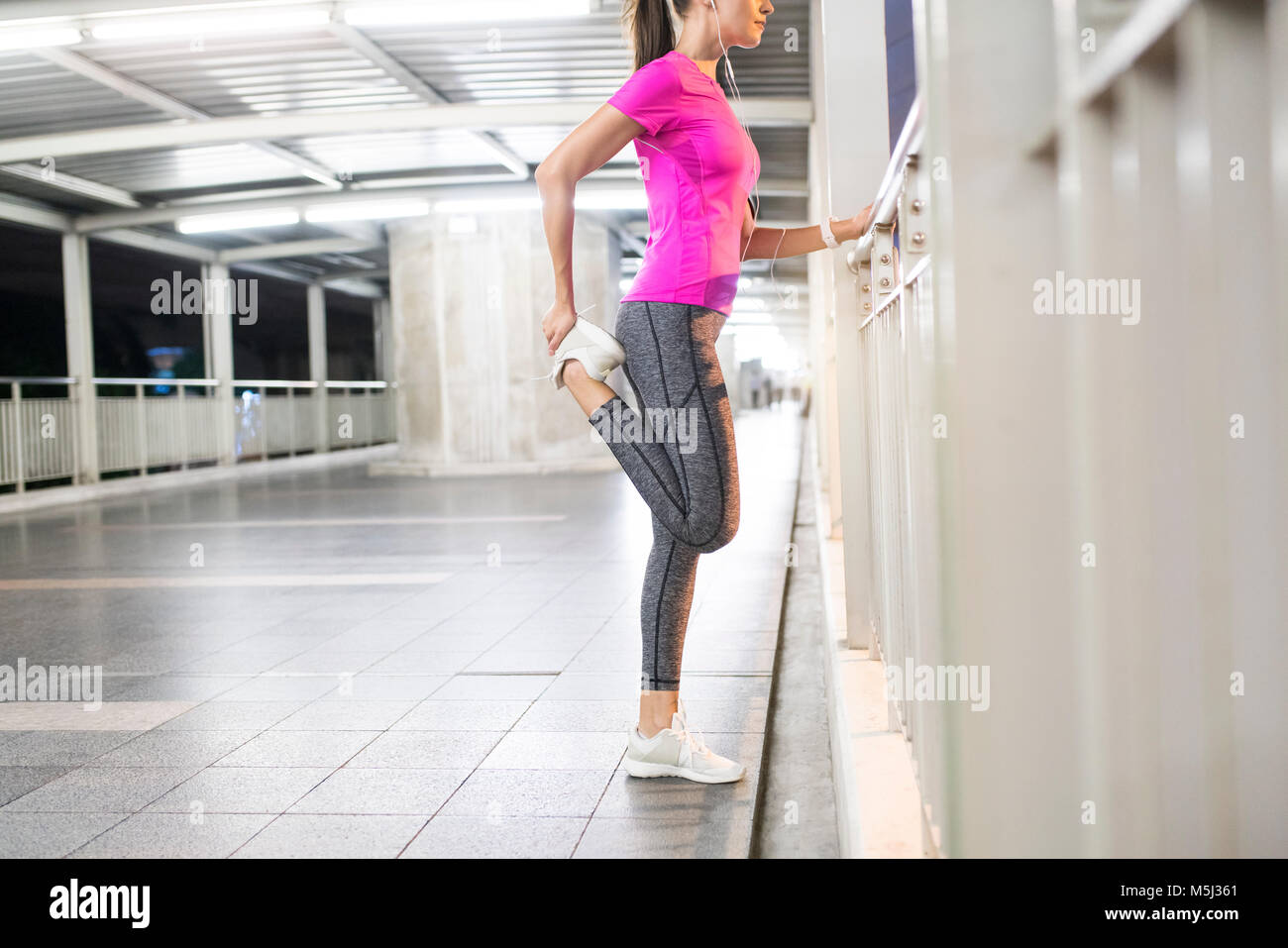 Giovane donna in rosa sportshirt stiramento nella moderna stazione della metropolitana di notte Foto Stock