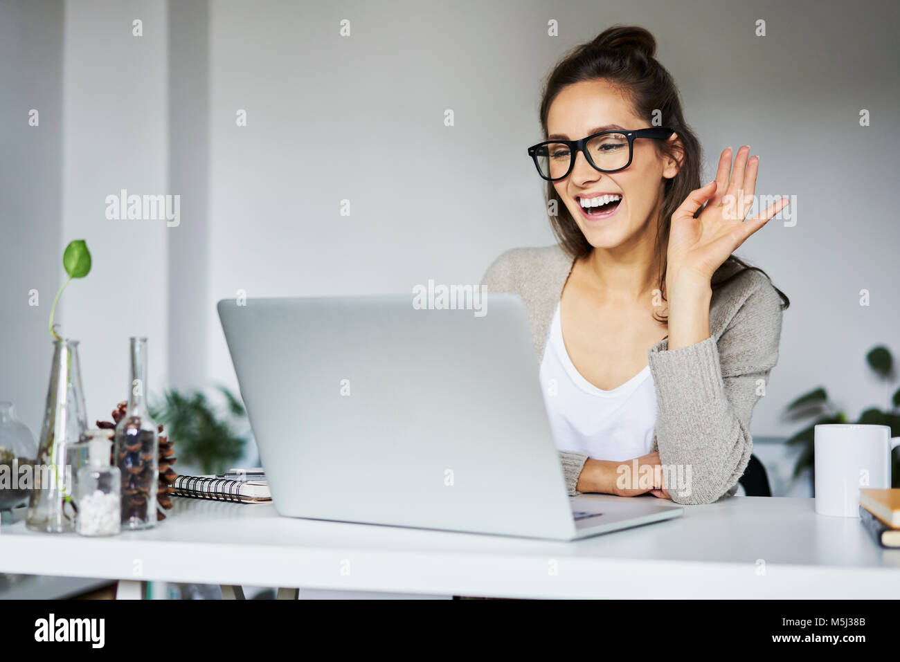 Giovane donna ridendo durante la video chat alla scrivania Foto Stock