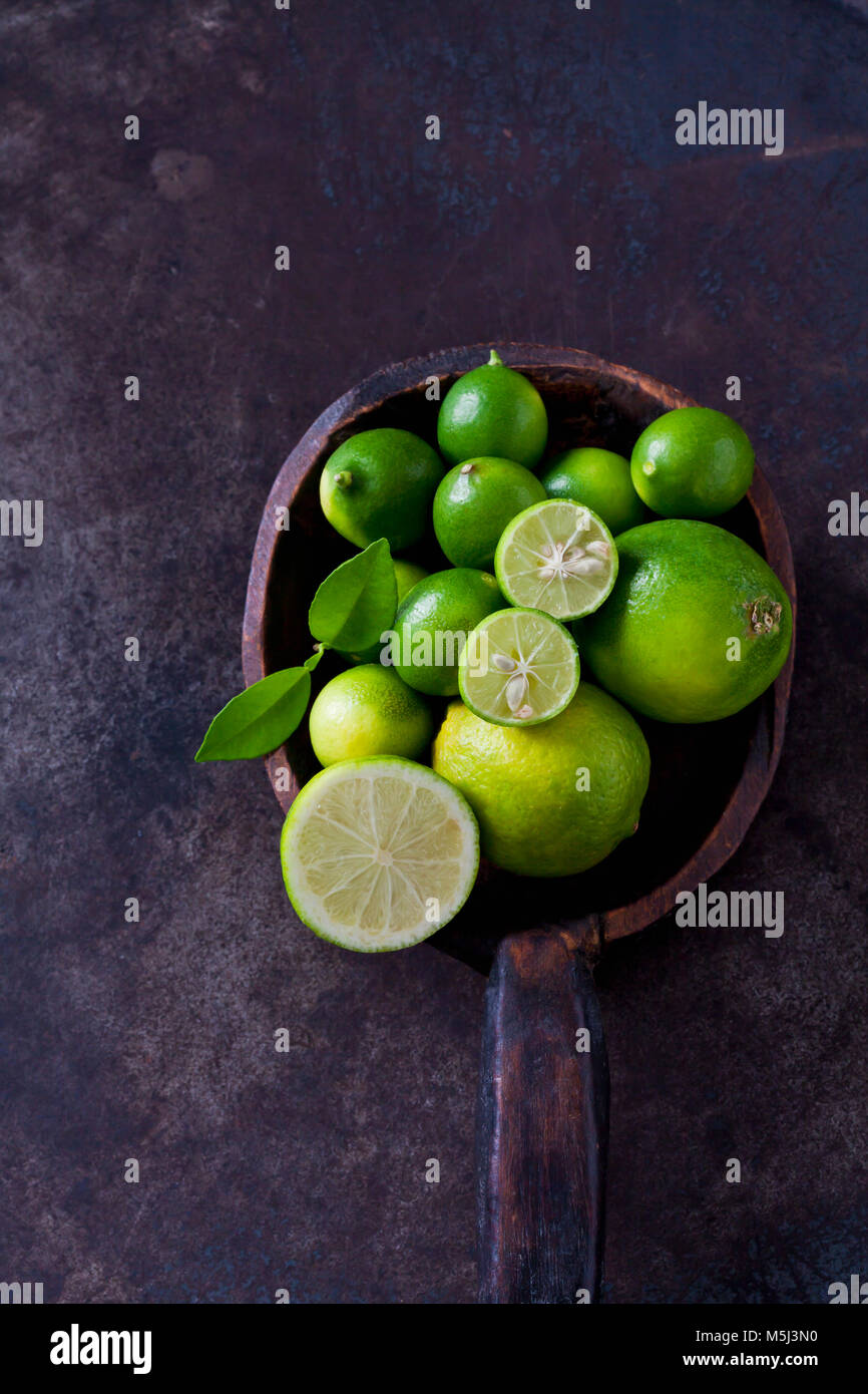 Il cucchiaio di legno con affettato e intera limequats, lime e foglie sul terreno arrugginito Foto Stock