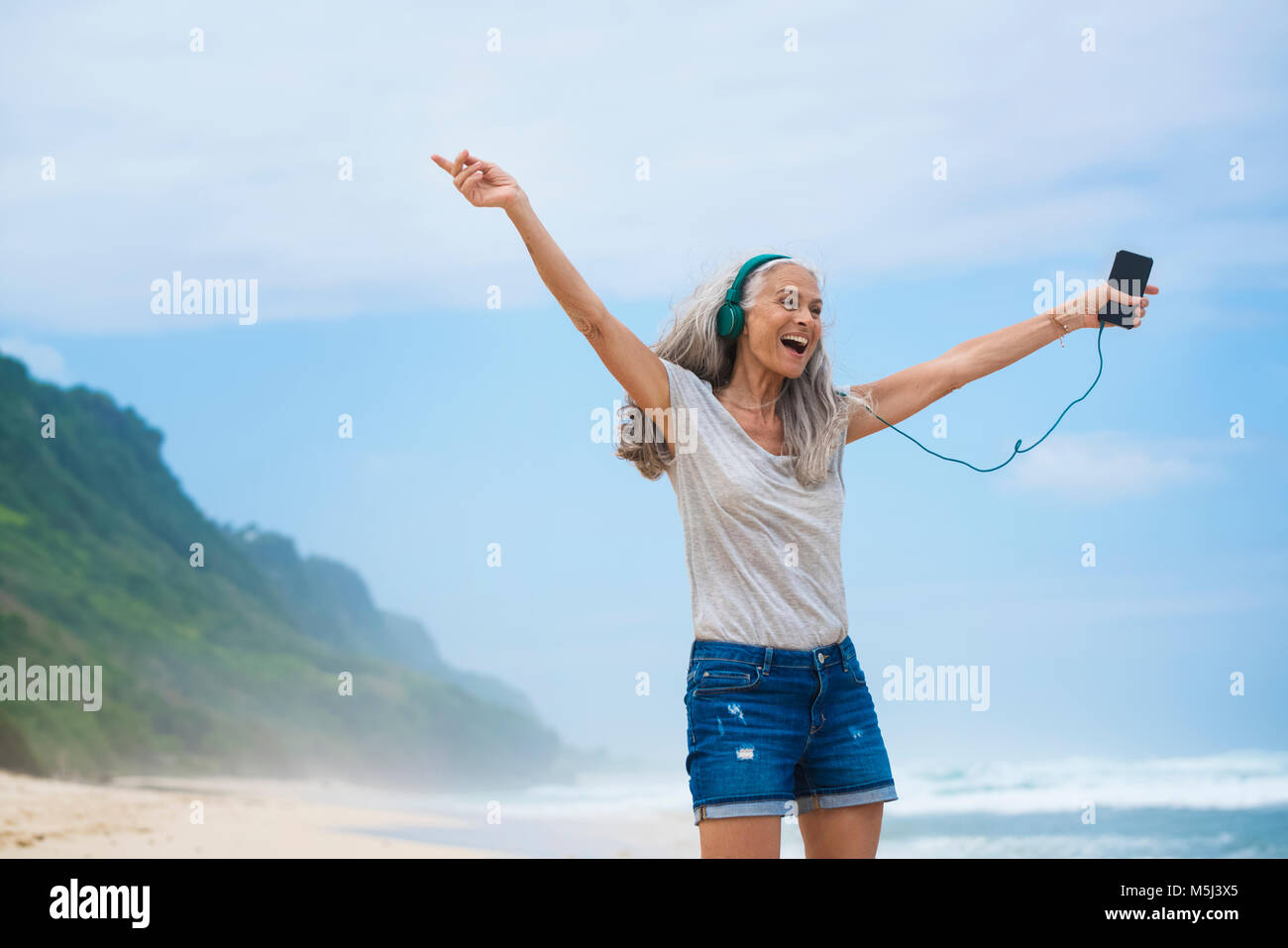 Donna senior con cuffie balli sulla spiaggia Foto Stock