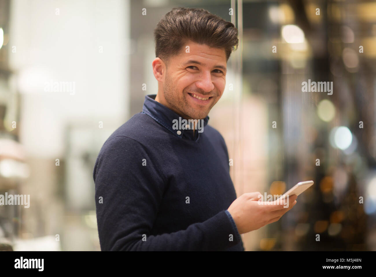Ritratto di laughing man con il cellulare in un centro commerciale per lo shopping Foto Stock