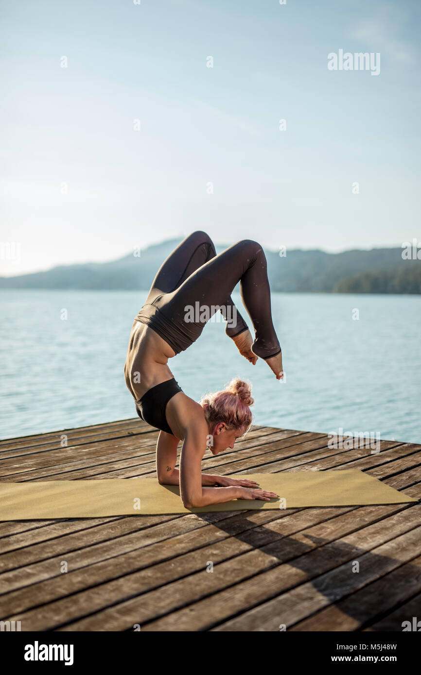 La donna a praticare yoga sul pontile di un lago Foto Stock