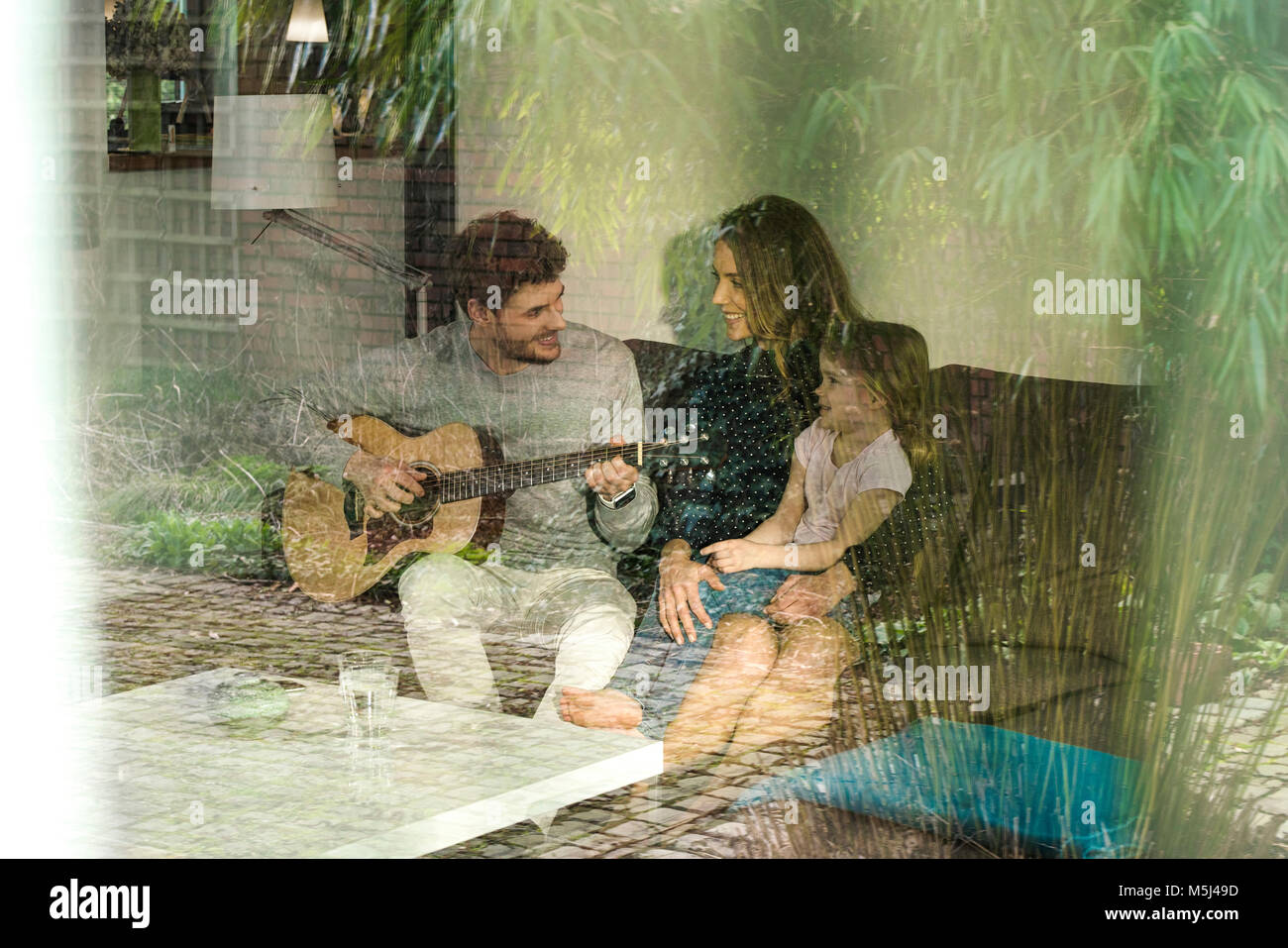 Genitori felici e la figlia a suonare la chitarra sul divano di casa Foto Stock