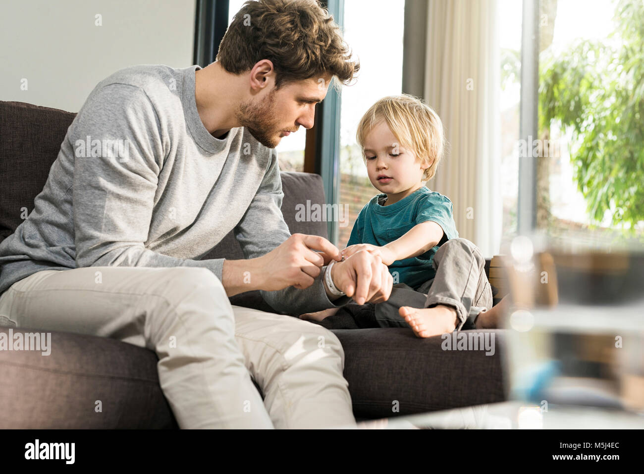 Esaminando il figlio del padre smartwatch sul lettino a casa Foto Stock