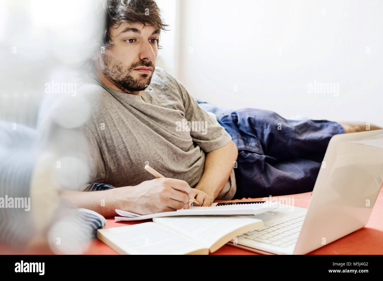 Ritratto di studente giacente sul letto con il computer portatile e il libro Imparare Foto Stock