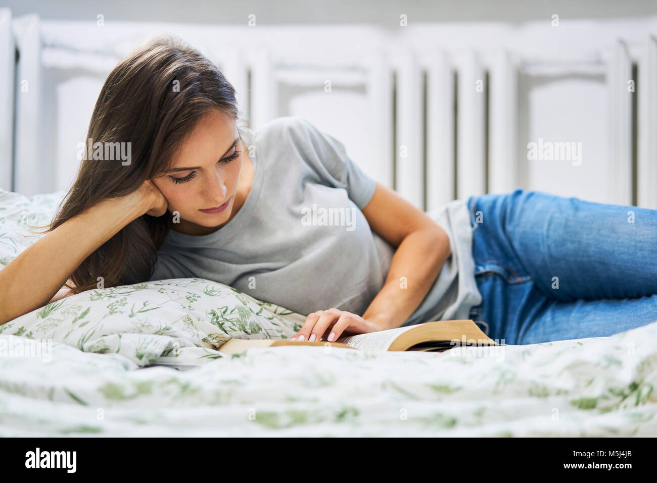 Giovane donna di casa giacente in letto libro di lettura Foto Stock