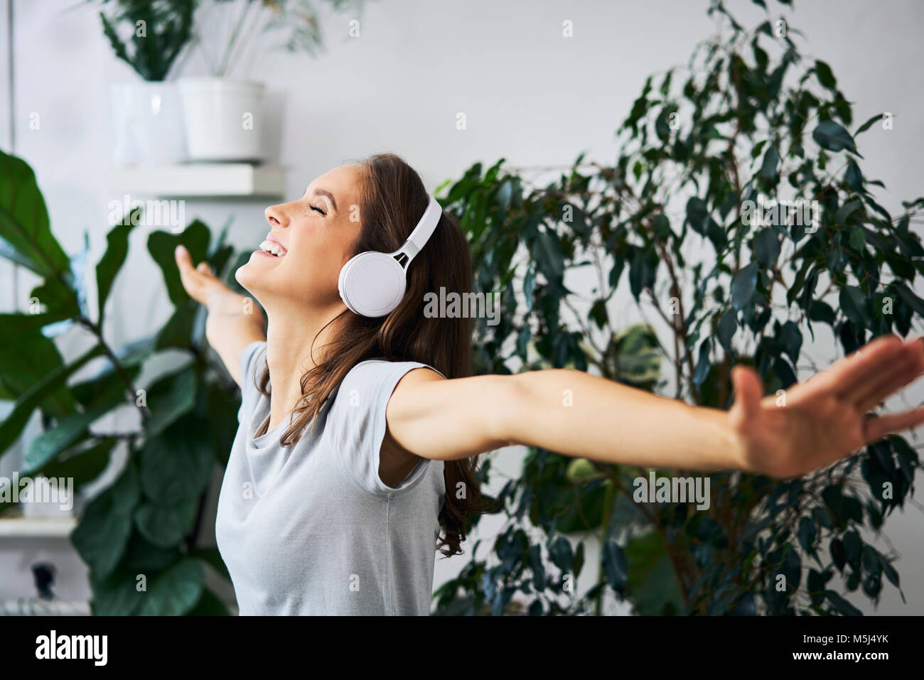 Felice giovane donna con bracci oustretched ascoltare musica ad impianto indoor Foto Stock