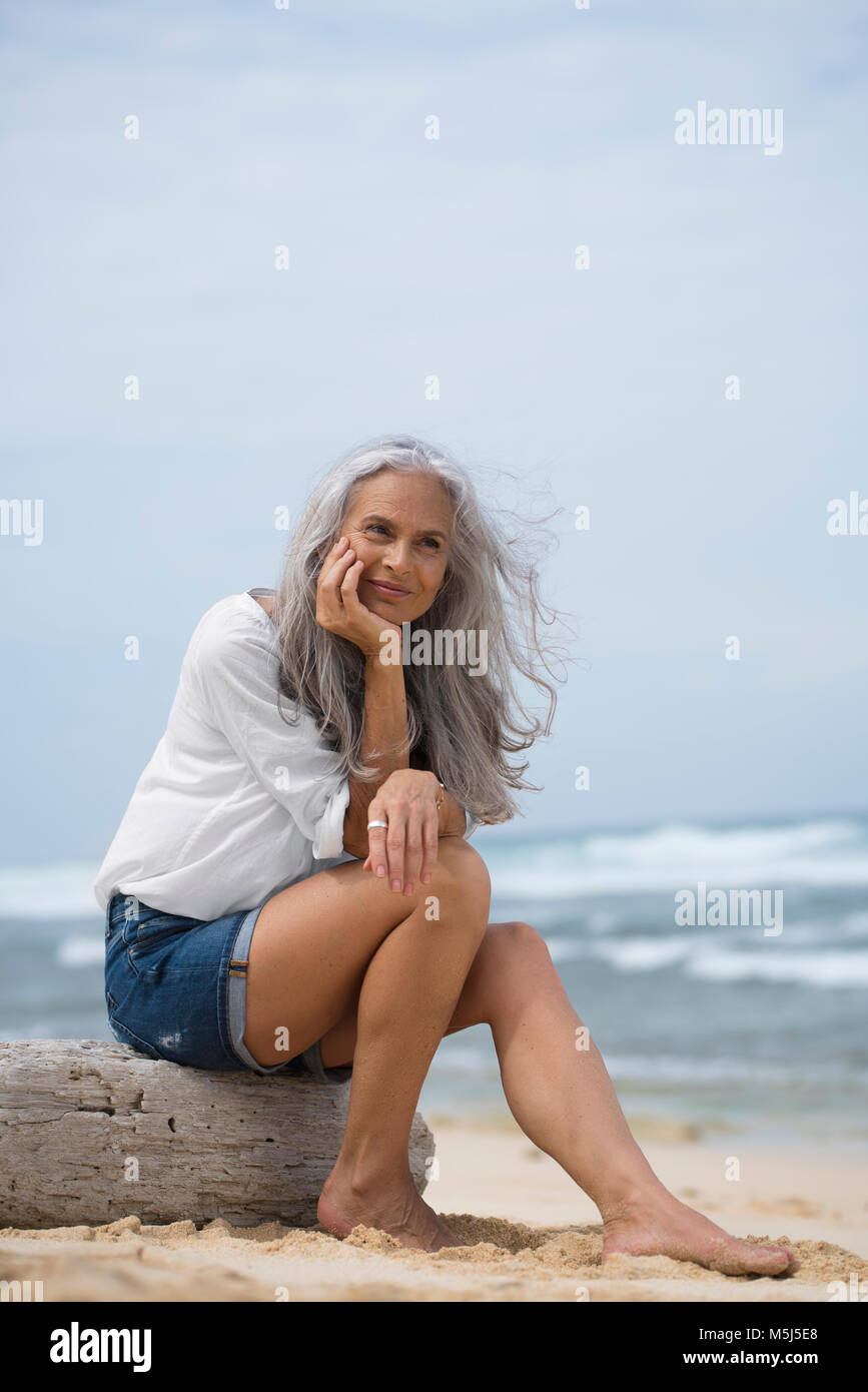 Senior bella donna seduta in spiaggia Foto Stock