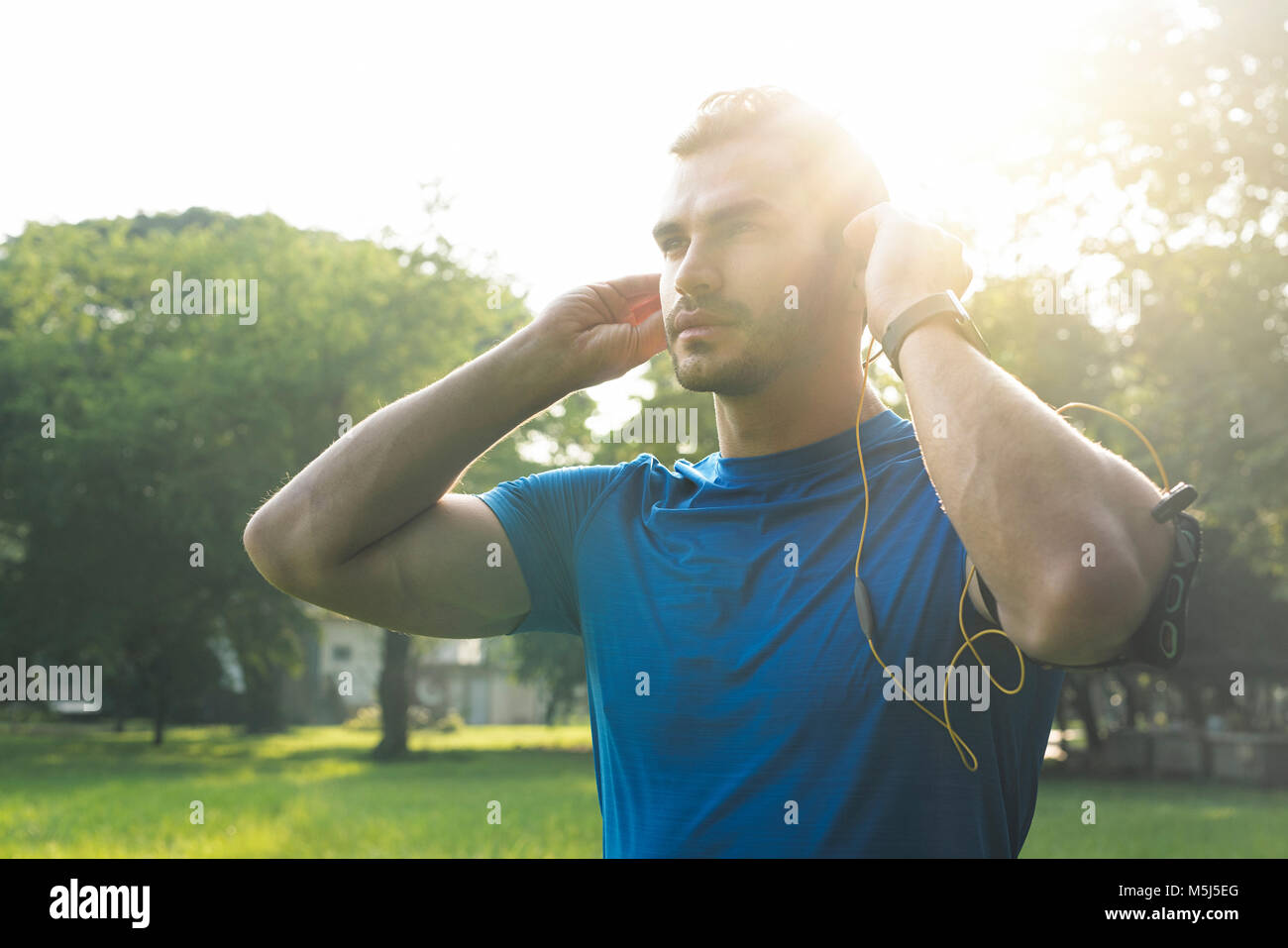 Uomo sportivo indossando le cuffie, preparazione per la formazione nel parco urbano Foto Stock