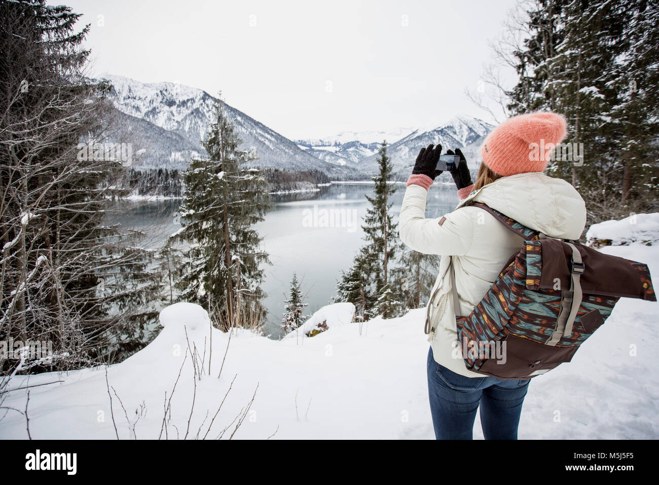 Giovane donna di scattare una foto in inverno alpino paesaggio con lago Foto Stock