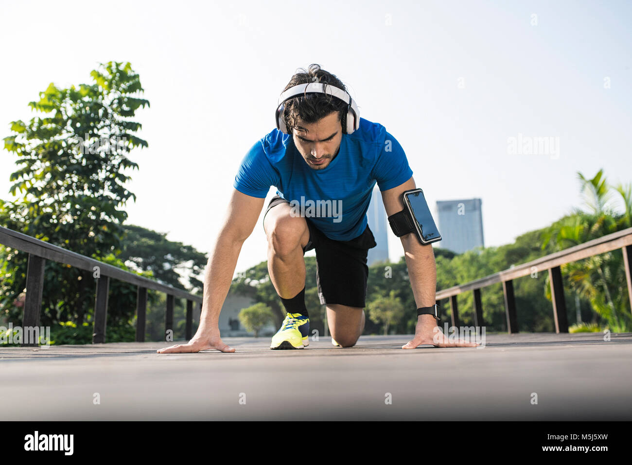 Formazione Runner posizione iniziale sulla strada nel parco urbano, indossando le cuffie Foto Stock