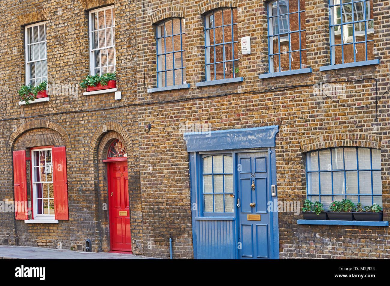 Una bella fila di mattoni casa a schiera con il rosso e il blu delle porte, persiane rosse in corrispondenza di una finestra e finestre a Southwark Londra Foto Stock