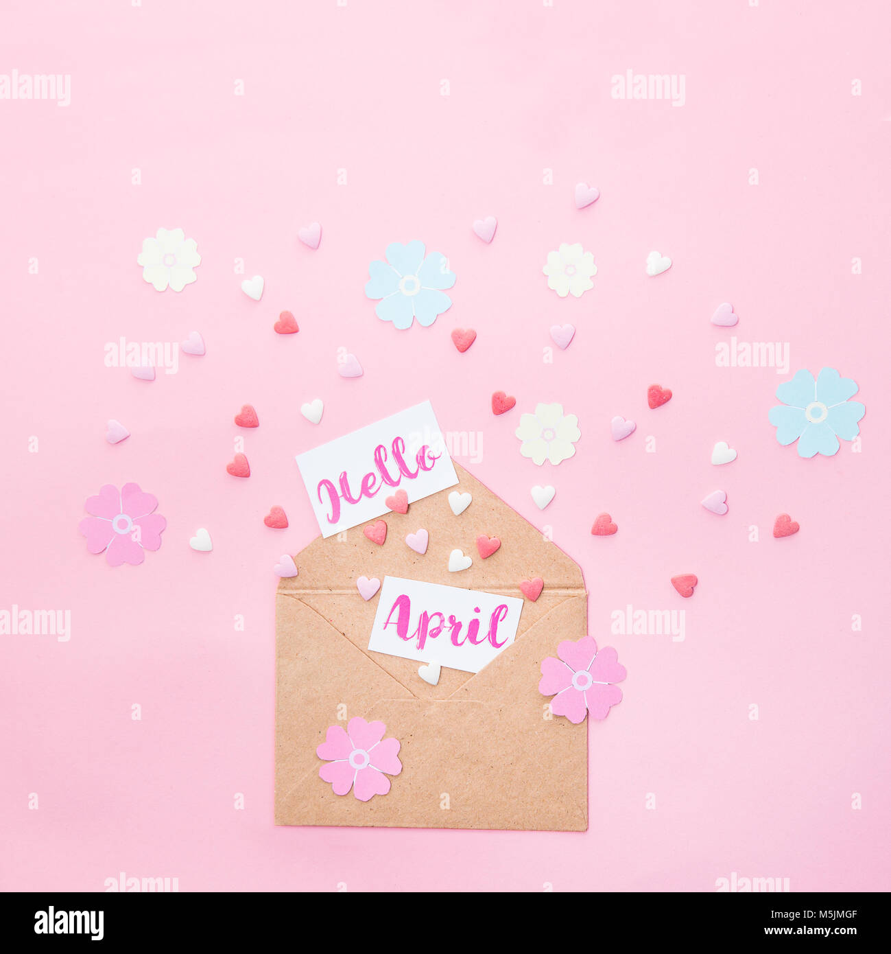 Multicolor dolci zucchero candito cuori, artigianato fiori di carta e carte con Ciao aprile lettering volare al di fuori della carta craft busta su sfondo rosa Foto Stock