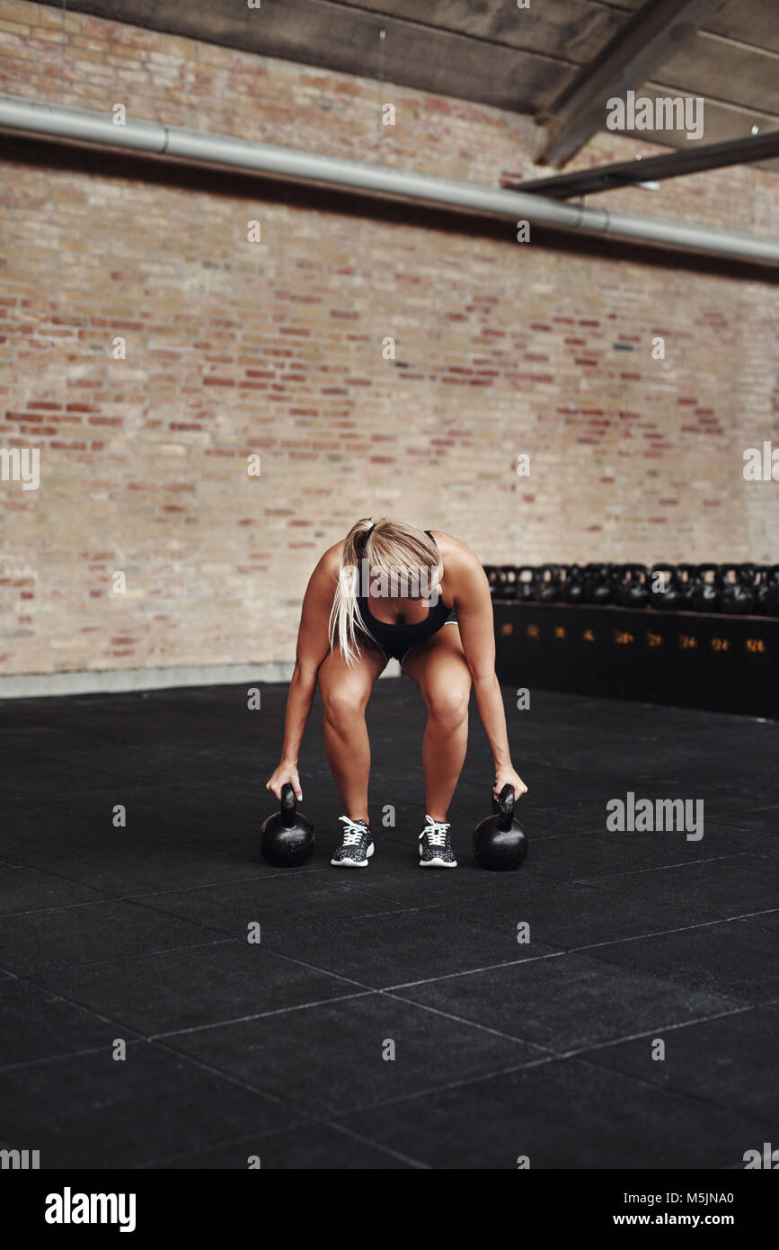 Montare la giovane donna bionda in palestra abbigliamento lavoro fuori da solo con i pesi del pavimento di un club di salute Foto Stock