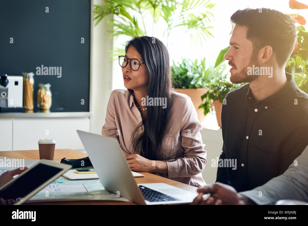 Diversi colleghi parlano seduti insieme ad un tavolo per riunioni in un ufficio avente una riunione Foto Stock
