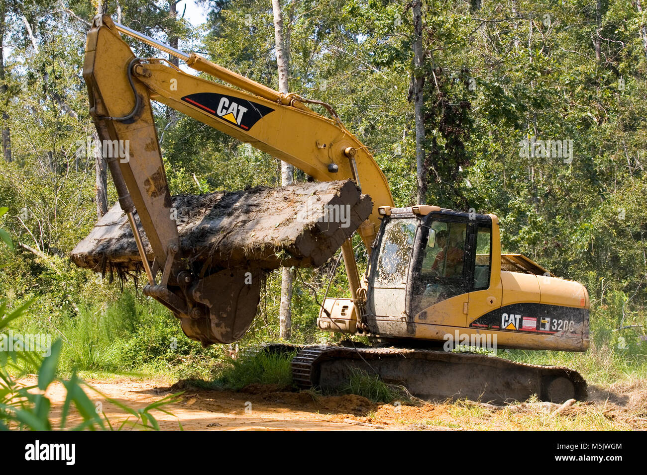 Cat 3200 trackhoe pesanti in movimento gru legno tappetini lungo una registrazione di ghiaia strada in Alabama River palude. Foto Stock