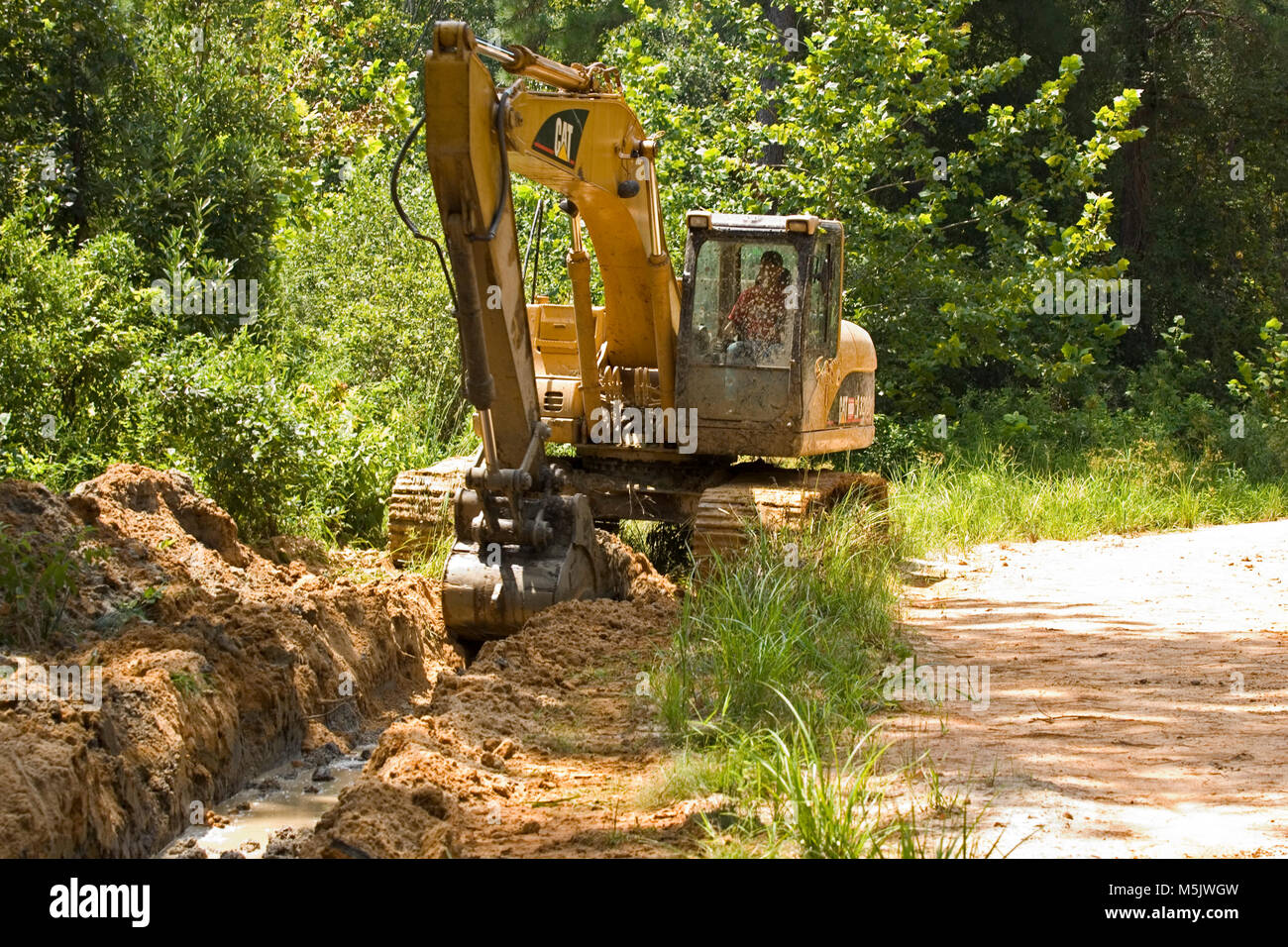 Cat 3200 trackhoe (via zappa, escavatore meccanico a pala) lo scavo di una fossa di scolo lungo una registrazione di ghiaia strada in Alabama River palude, in banner Foto Stock