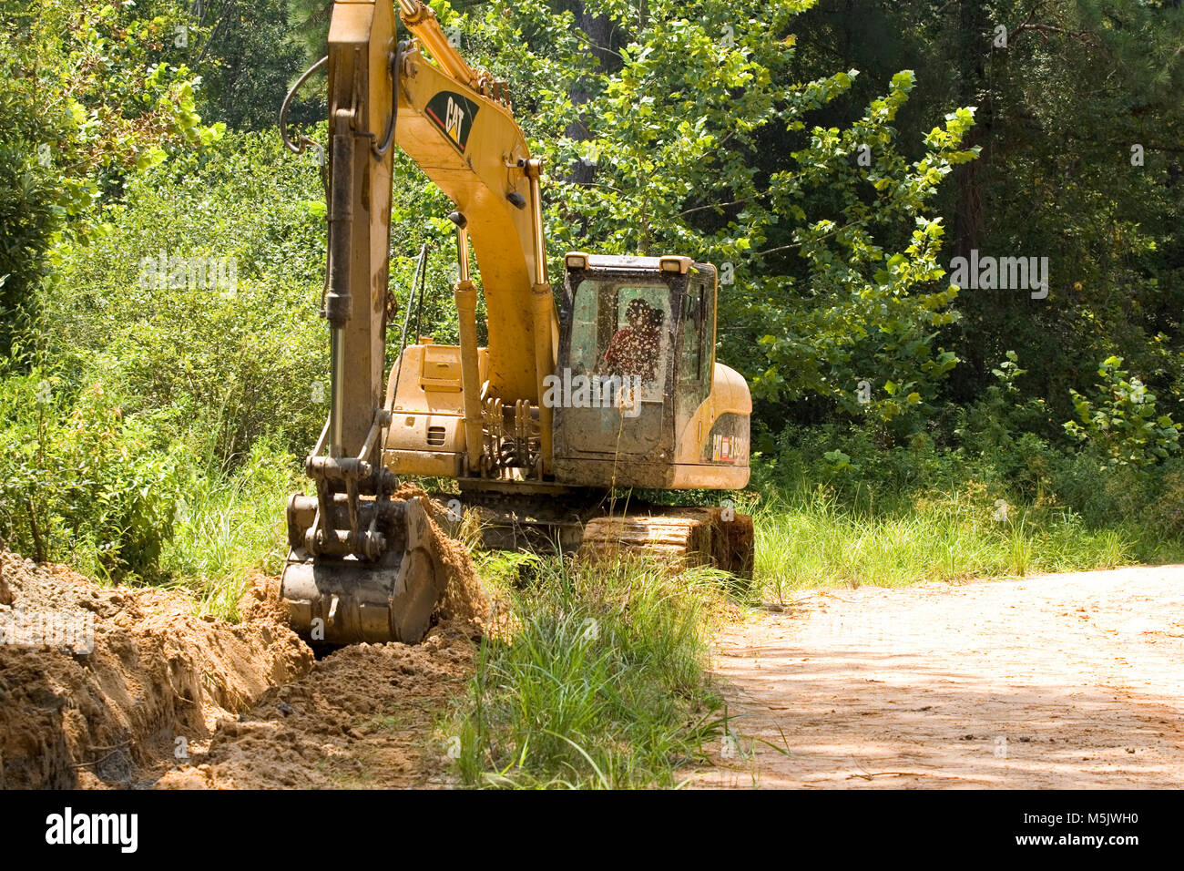 Cat 3200 trackhoe (via zappa, escavatore meccanico a pala) lo scavo di una fossa di scolo lungo una registrazione di ghiaia strada in Alabama River palude, in banner Foto Stock