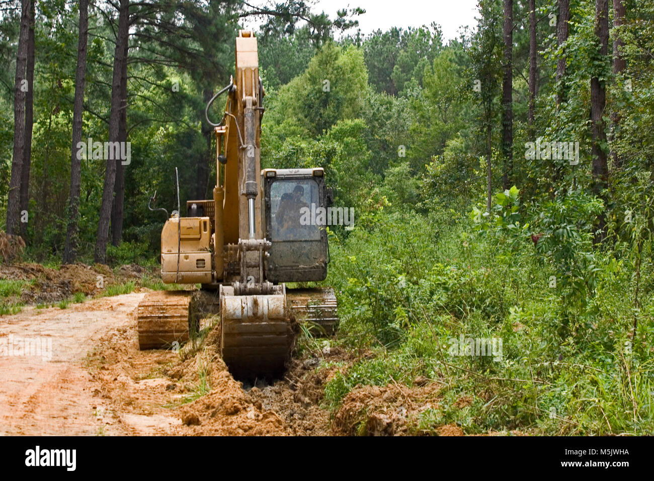 Cat 3200 trackhoe (via zappa, escavatore meccanico a pala) lo scavo di una fossa di scolo lungo una registrazione di ghiaia strada in Alabama River palude, in banner Foto Stock