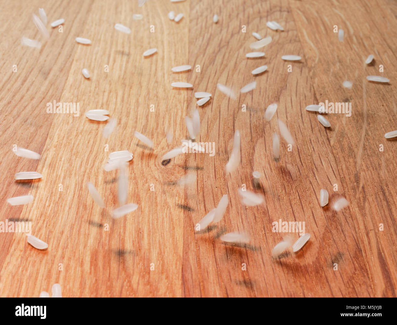 Bianco di riso greggio che cade sul legno marrone con sfondo sfocatura del movimento Foto Stock