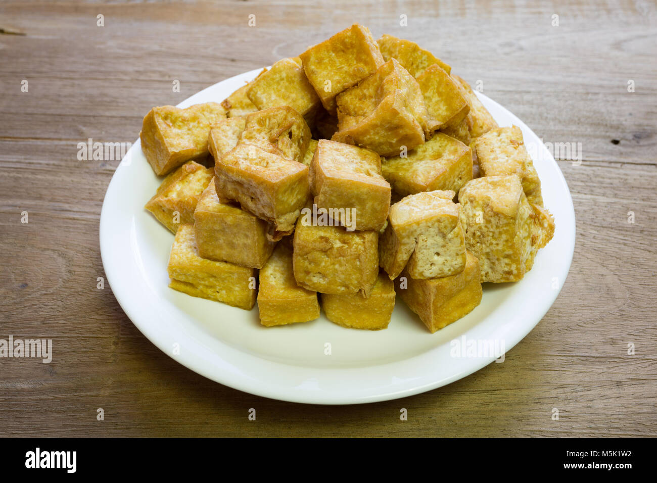 Dolce fritto i cubetti di tofu in piastra bianca su sfondo di legno Foto Stock