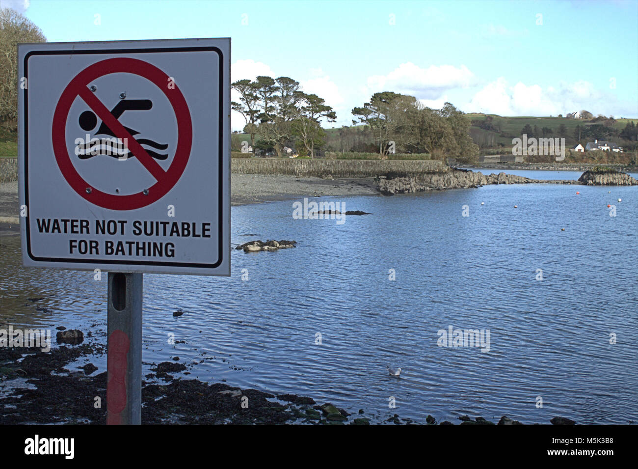 Segnale di avvertimento a causa di inquinamento di effluente in una pittoresca baia da un emissario di liquame. Foto Stock