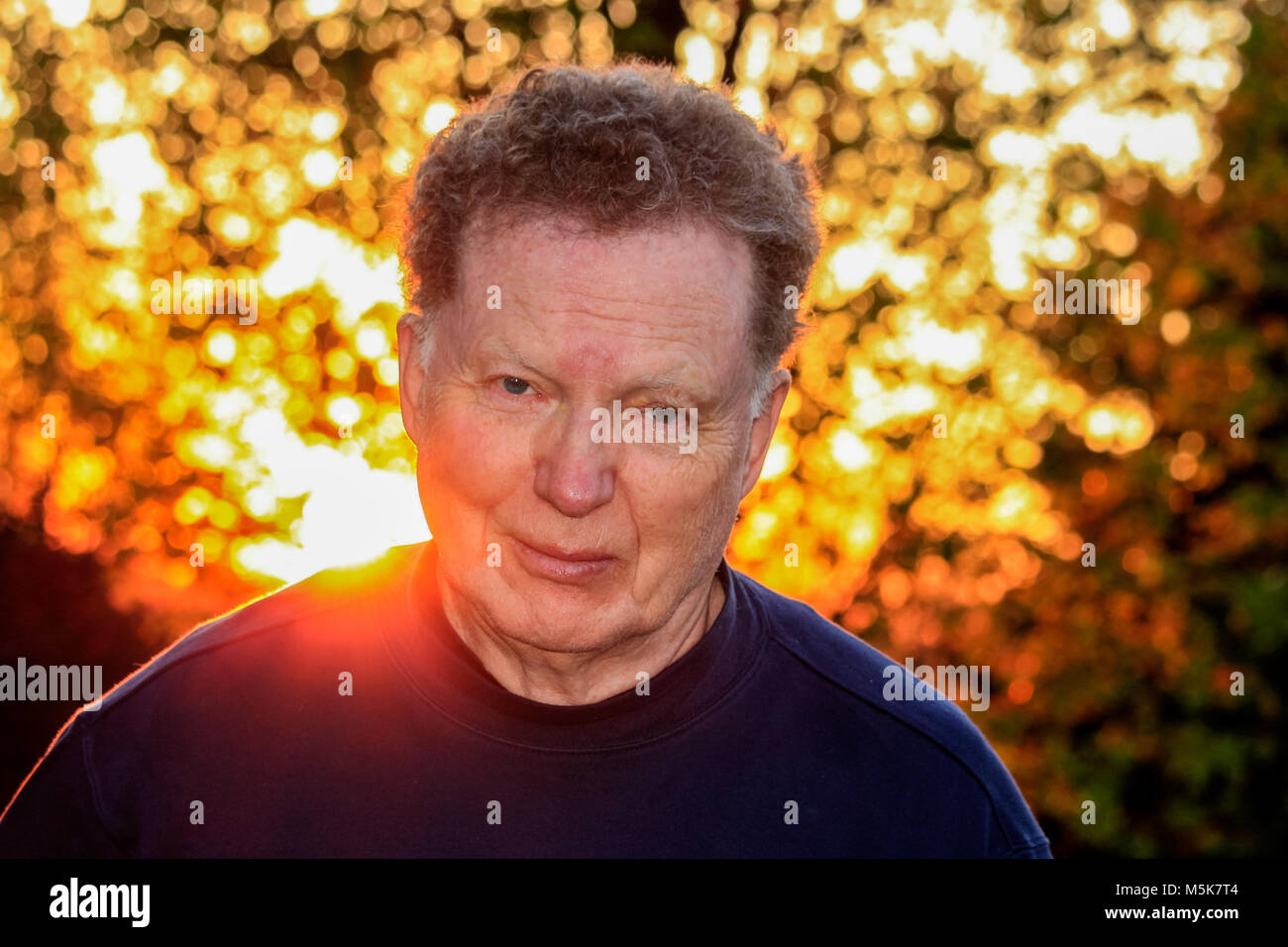 Colpo alla testa di un uomo anziano al tramonto in autunno; raggi del sole proveniente da dietro Foto Stock