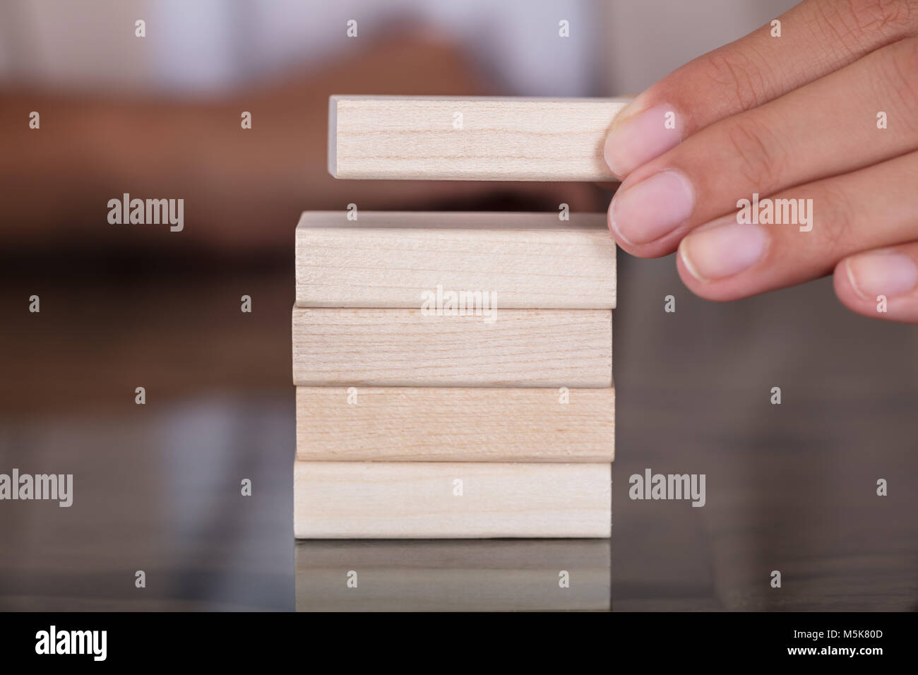 Close-up di imprenditrice mano posizionando il blocco di legno sulla torre di legno a tavola Foto Stock